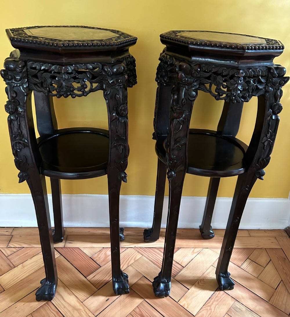 A pair of octagonal Chinese dark padouk wood plant stands with inset marble tops, pierced openwork aprons, lower shelves, and claw feet.