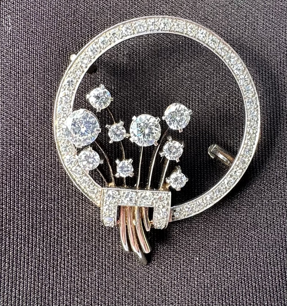 A circular platinum brooch set with small diamonds enclosing a floral spray motif of larger round diamonds.