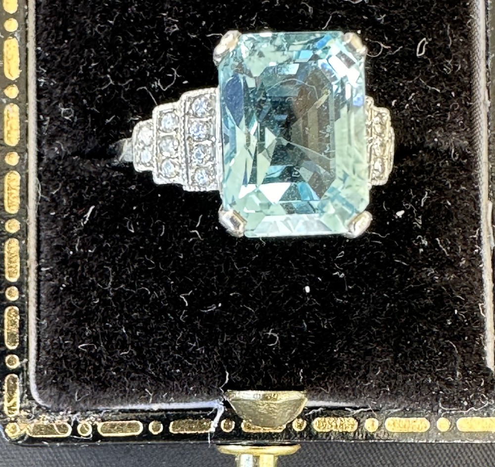 An Art Deco platinum ring featuring a central rectangular step-cut pale blue aquamarine flanked by stepped diamond-set shoulders.