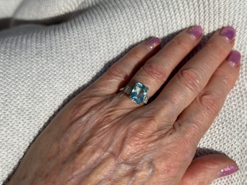 An Art Deco platinum ring featuring a central rectangular step-cut pale blue aquamarine flanked by stepped diamond-set shoulders. View IV