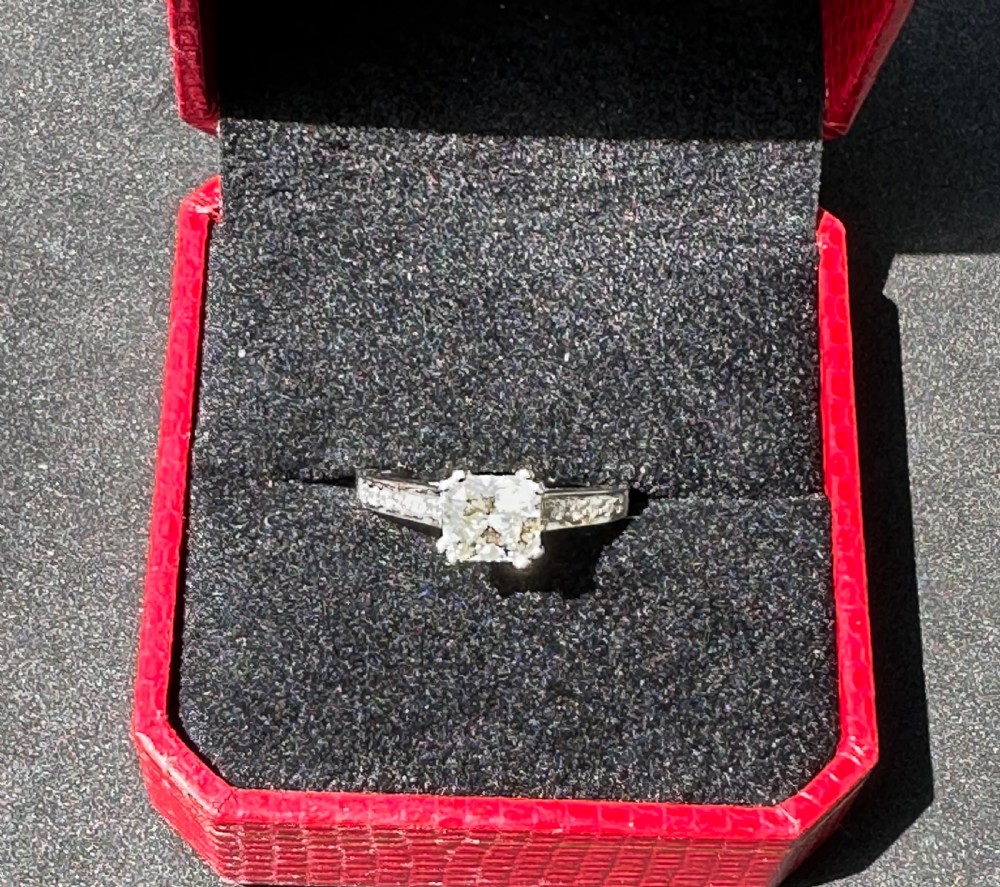 An 18ct gold solitaire ring featuring a central square-cut stone with accent stones set into the shoulders. View II