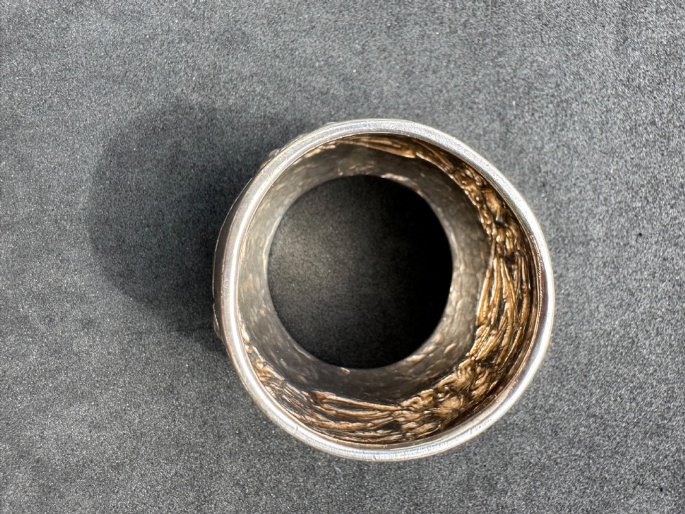 A hand-hammered sterling silver barrel-shaped napkin ring with an embossed relief band and rolled borders. View IV