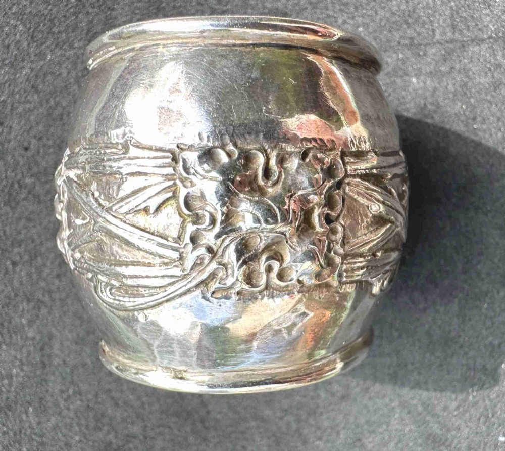 A hand-hammered sterling silver barrel-shaped napkin ring with an embossed relief band and rolled borders.