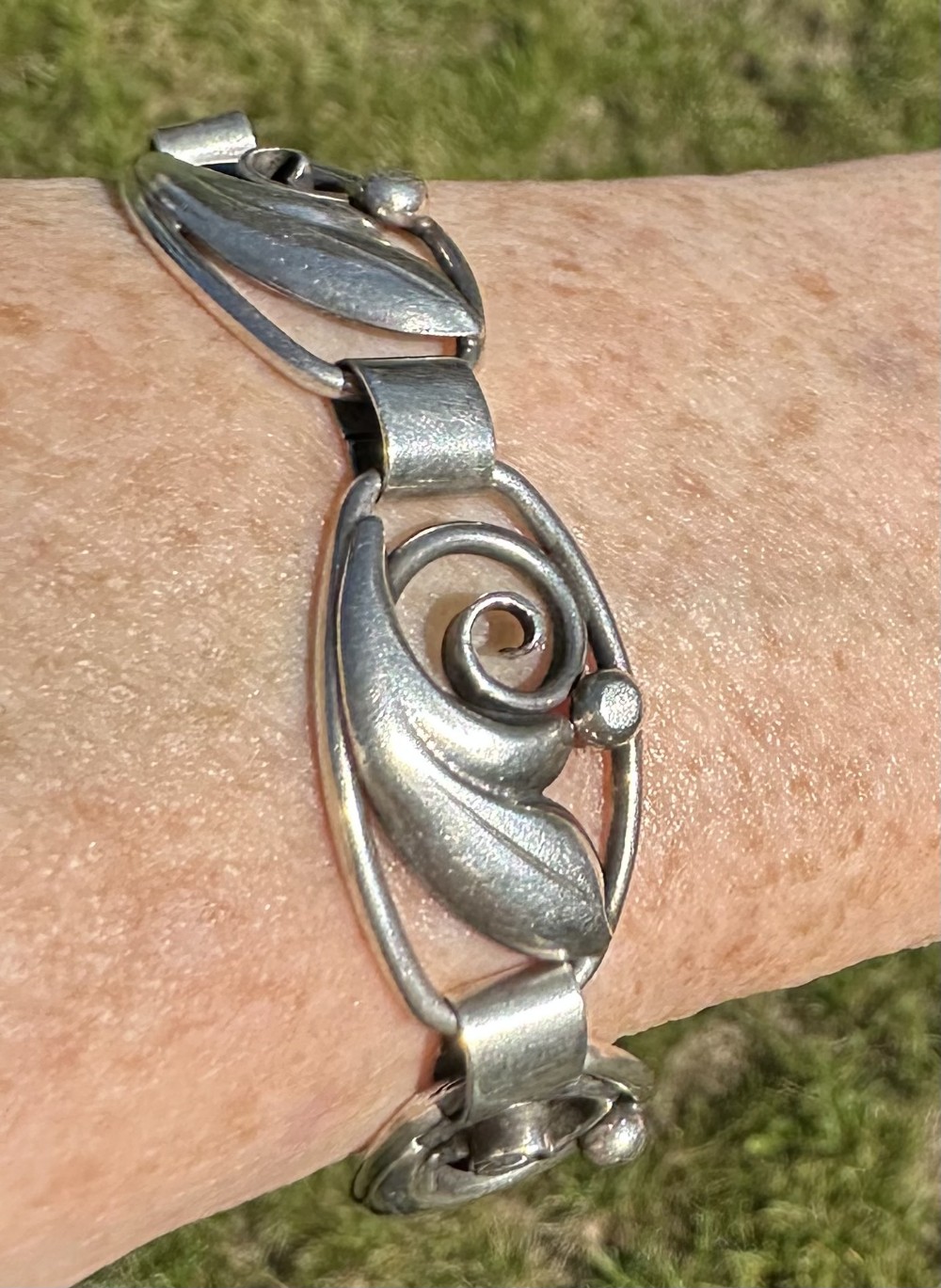 A Danish 830 silver link bracelet featuring oval openwork links with sculpted leaf forms, spiral scrolls, and bead accents.