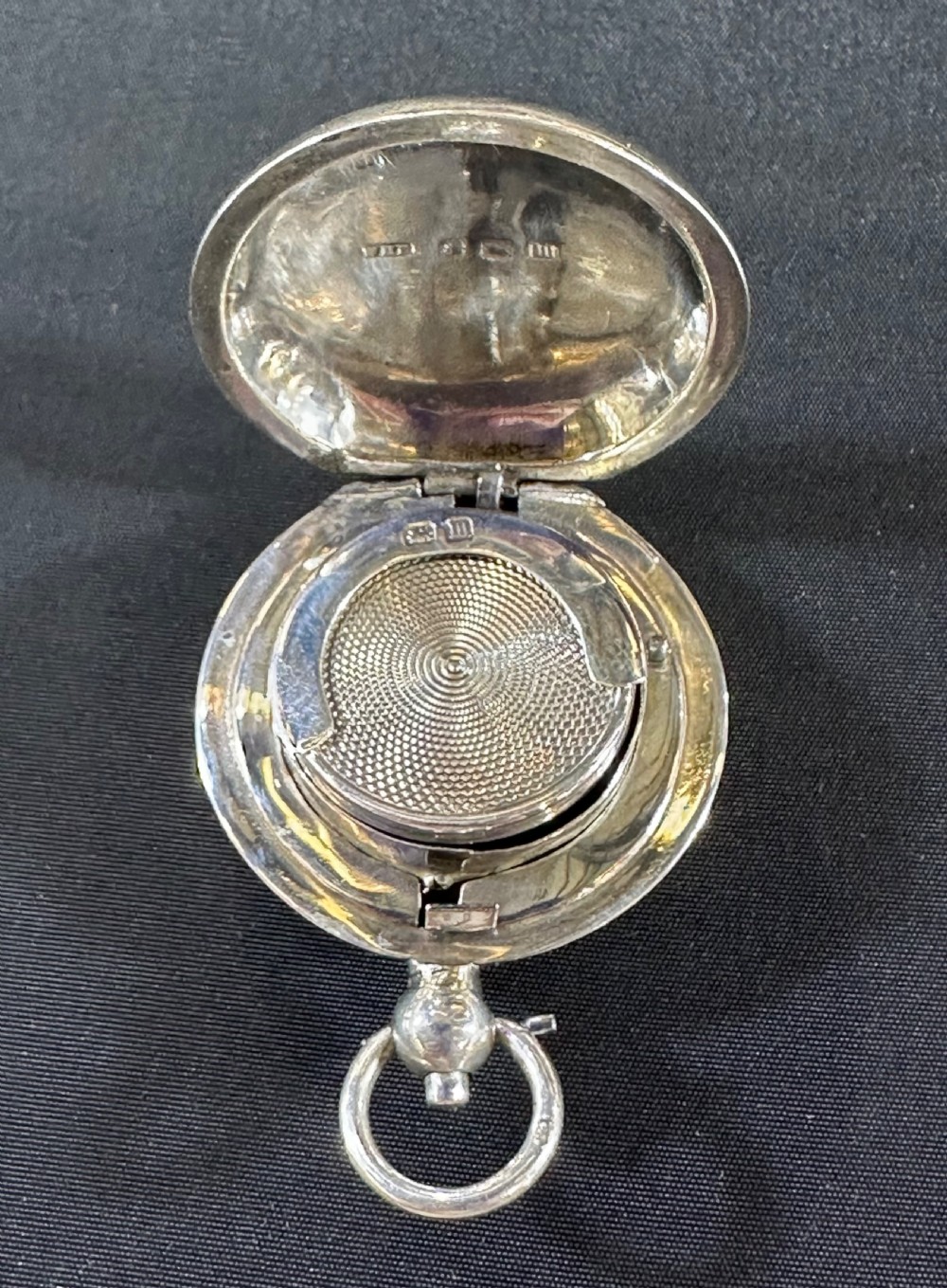An open Edwardian sterling silver circular sovereign case showcasing an internal engine-turned spring-loaded coin platform and silver hallmarks.