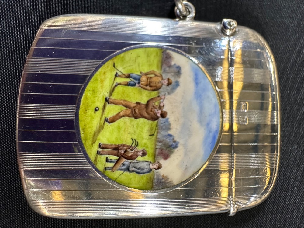 An engine-turned sterling silver vesta case featuring a central round enamelled plaque depicting three golfers on a golf course.