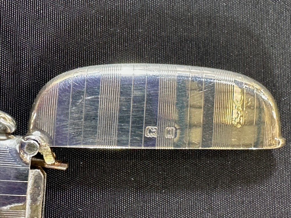 An engine-turned sterling silver vesta case featuring a central round enamelled plaque depicting three golfers on a golf course. View VI