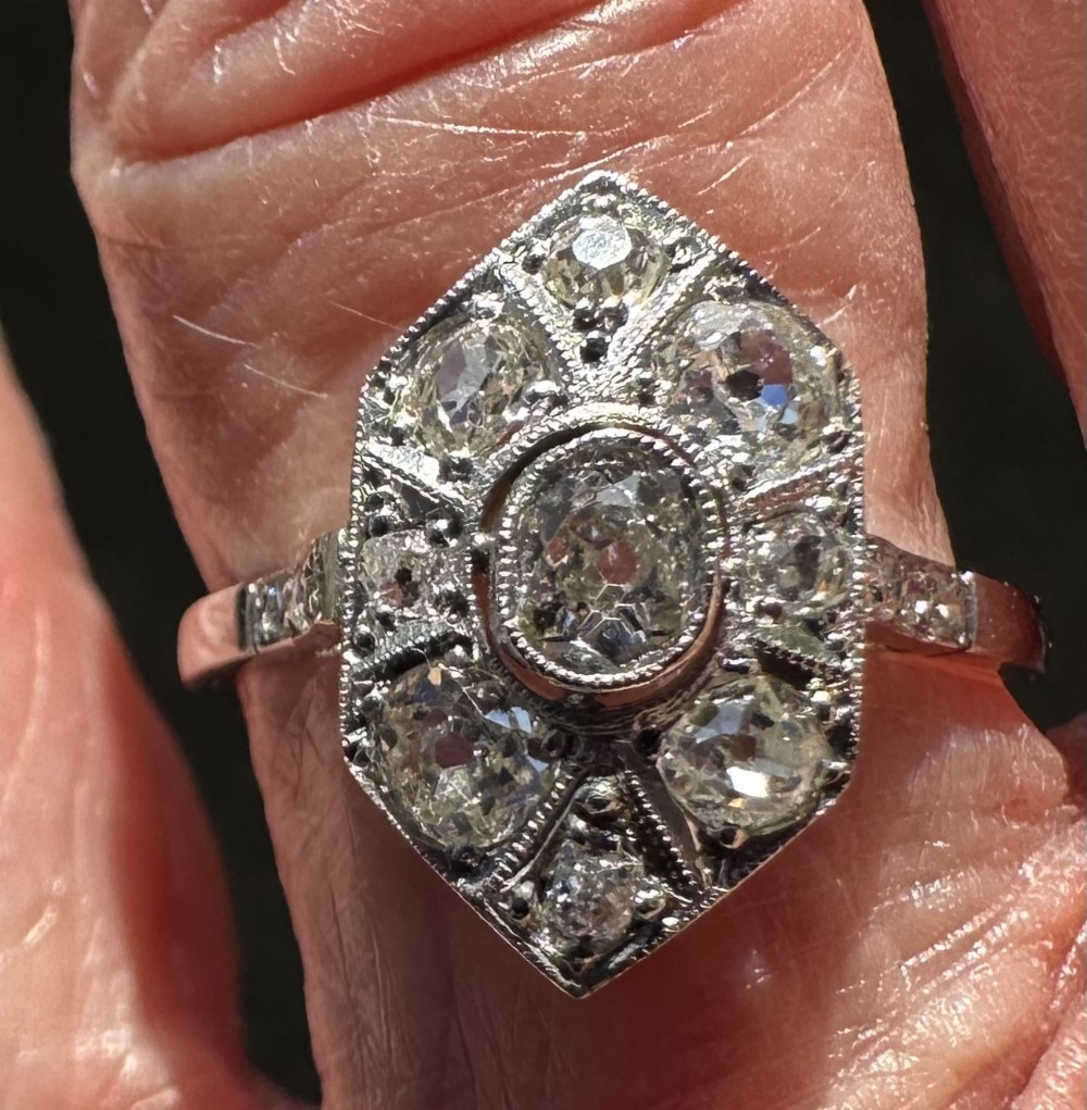 An Art Deco platinum ring featuring an elongated geometric plaque set with multiple round old cut diamonds and milgrain detailing.