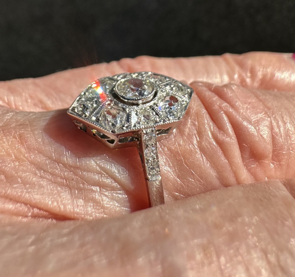 An Art Deco platinum ring featuring an elongated geometric plaque set with multiple round old cut diamonds and milgrain detailing. View IV