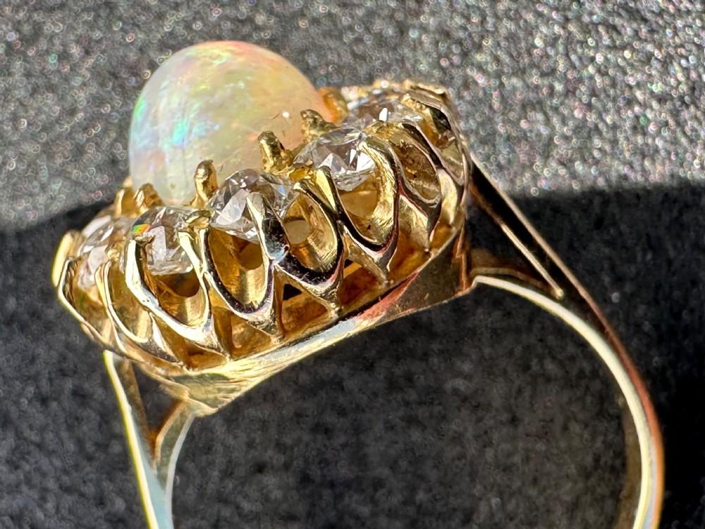An 18 carat yellow gold halo ring featuring an oval cabochon opal surrounded by a cluster of round diamonds. View II