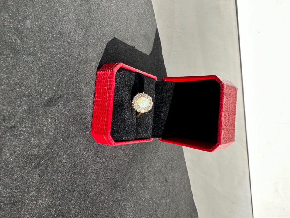 An 18 carat yellow gold halo ring featuring an oval cabochon opal surrounded by a cluster of round diamonds. View VII