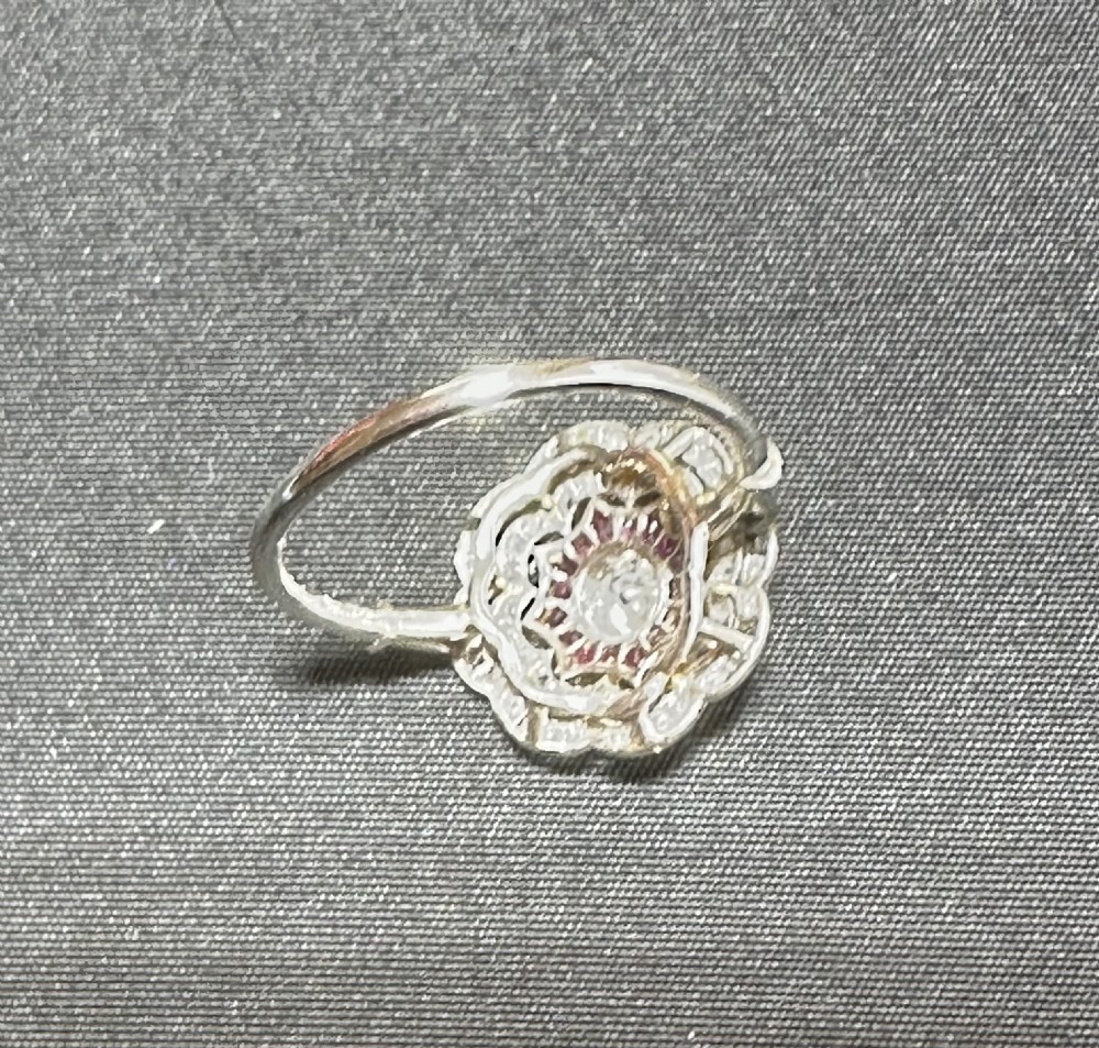 An Edwardian platinum cluster ring featuring a central round diamond encircled by a star-shaped border of calibre-cut red rubies and a scalloped diamond halo. View IV