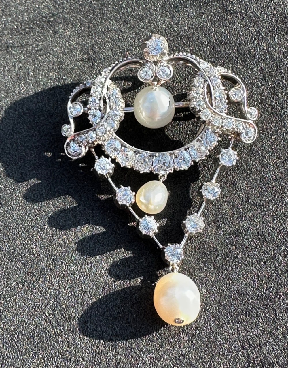 A platinum openwork pendant brooch featuring diamond-set scrollwork and three suspended natural pearl drops.
