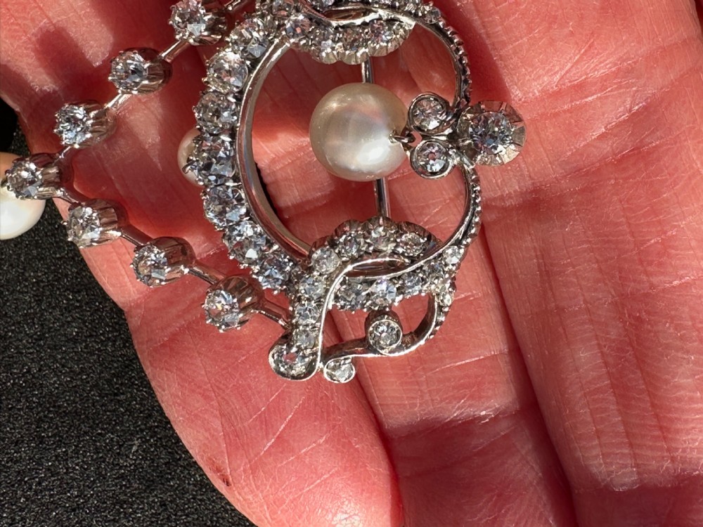 A platinum openwork pendant brooch featuring diamond-set scrollwork and three suspended natural pearl drops. View V