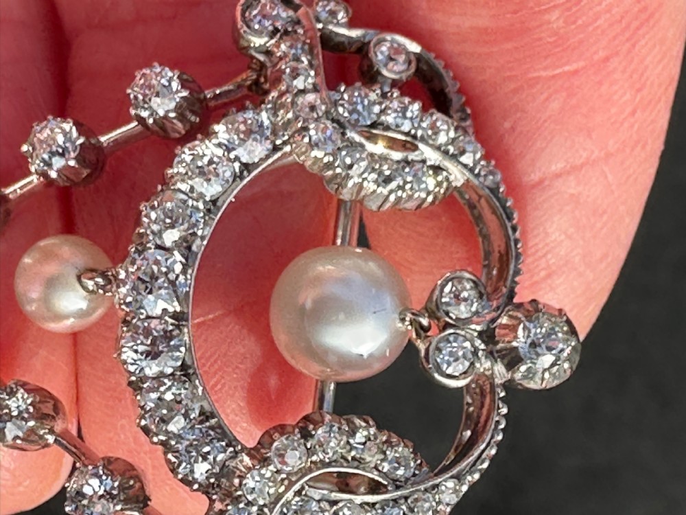 A platinum openwork pendant brooch featuring diamond-set scrollwork and three suspended natural pearl drops. View VI