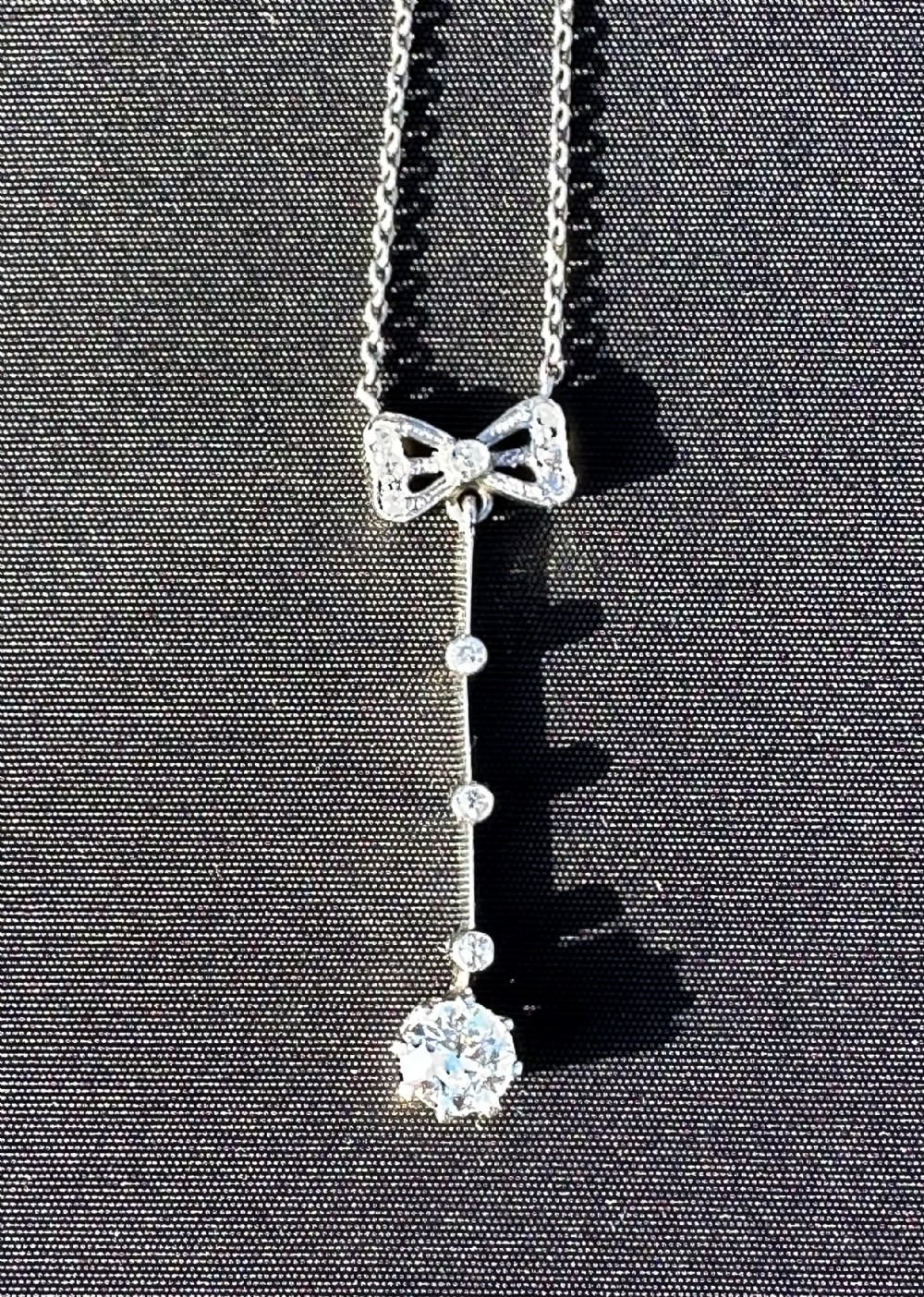 A 14ct white gold pendant featuring a diamond-set bow motif positioned above a vertical bar drop terminating in a round diamond.