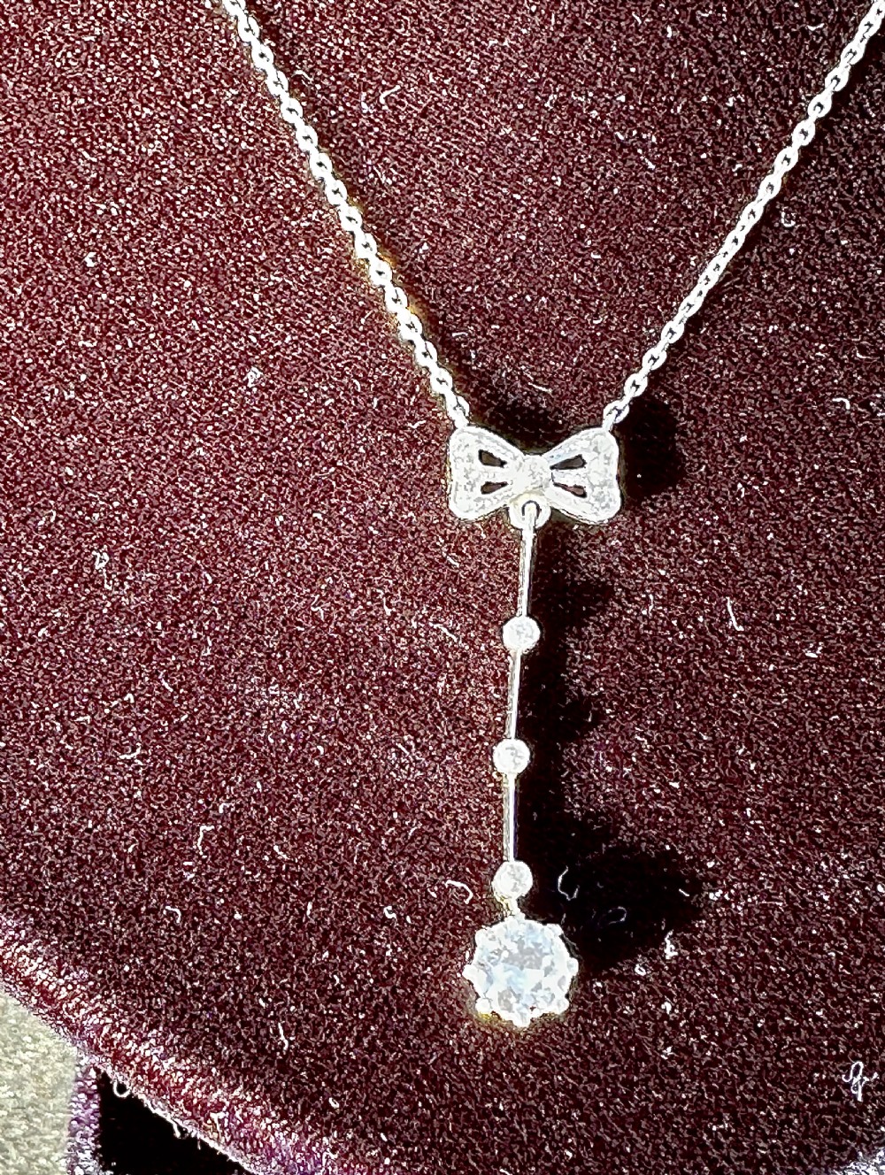 A 14ct white gold pendant featuring a diamond-set bow motif positioned above a vertical bar drop terminating in a round diamond. View III