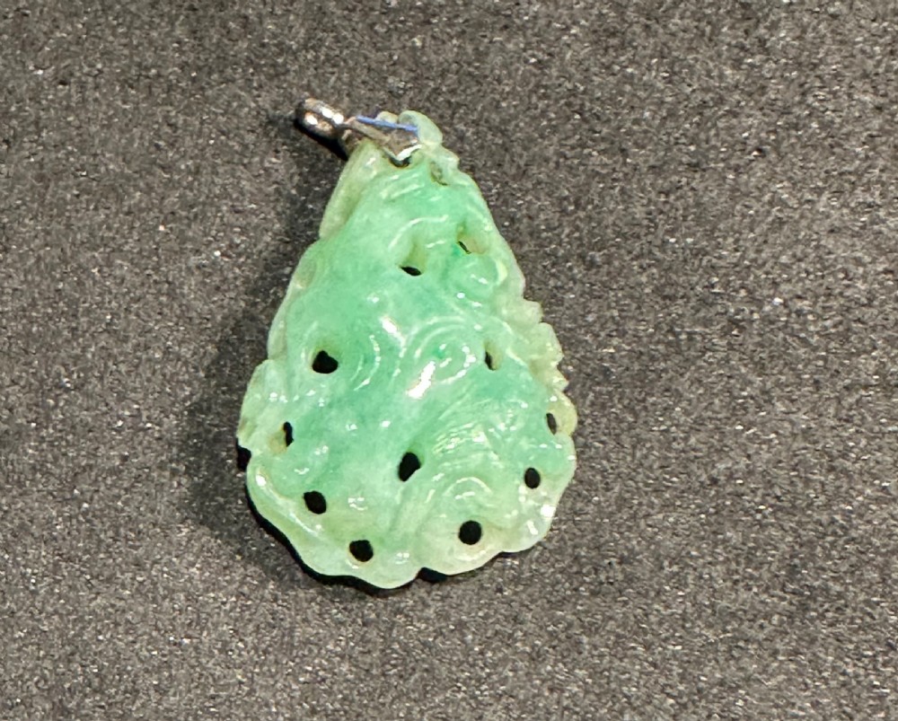 A light green carved jade pendant featuring openwork scroll patterns suspended from a metallic bail.