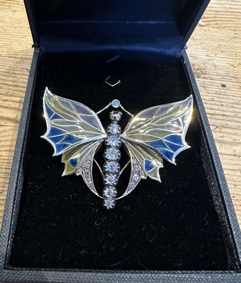 An Art Nouveau style butterfly brooch featuring blue and yellow plique-a-jour enamel wings with a diamond-paved body and gold framework.