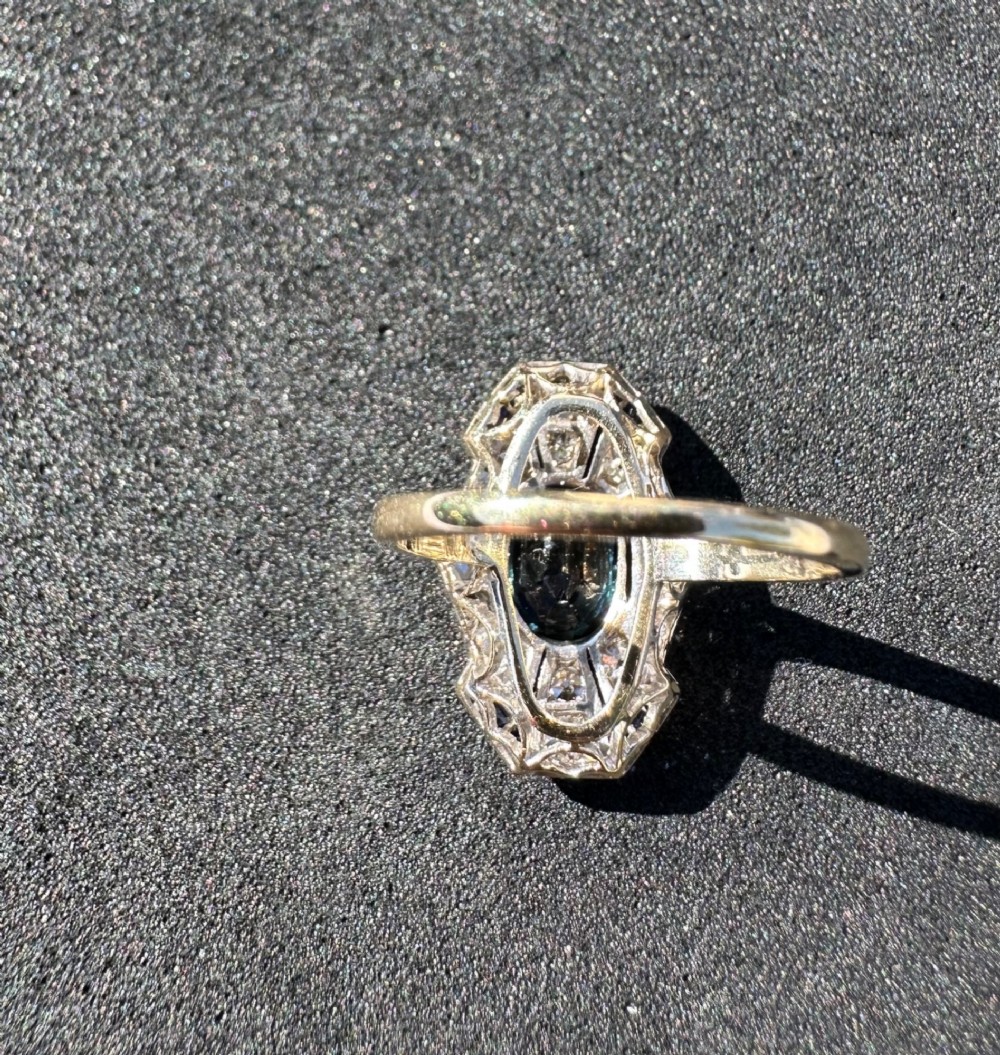 An Art Deco geometric panel ring featuring a central oval blue sapphire surrounded by diamonds and calibre-cut sapphire accents in a white metal and gold setting. View IV