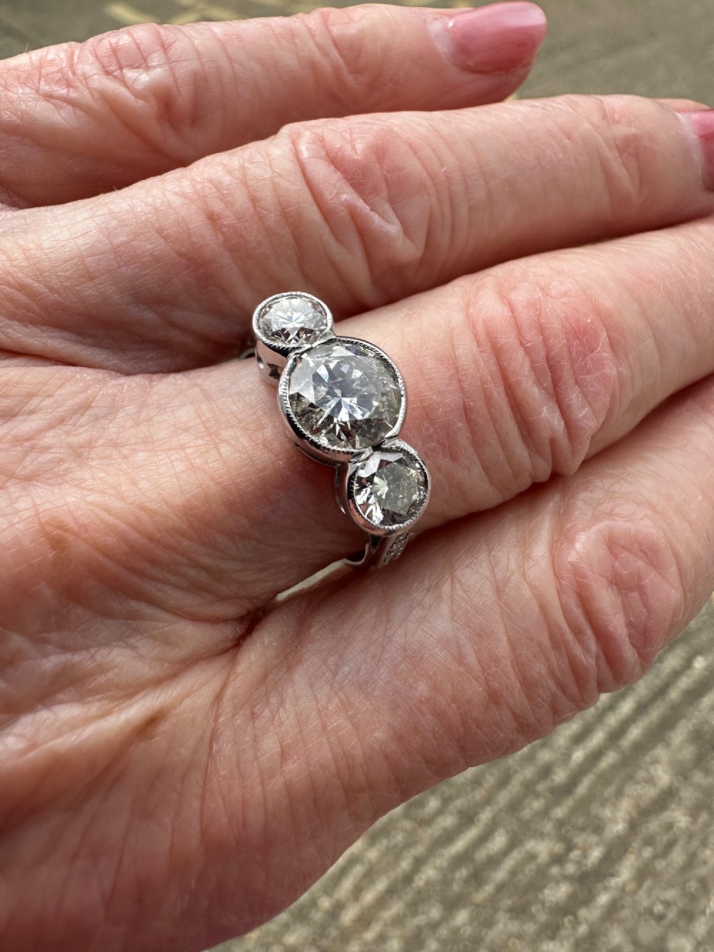 An 18ct white gold trinity ring featuring three round brilliant diamonds in rub-over bezel settings with millegrain edging.