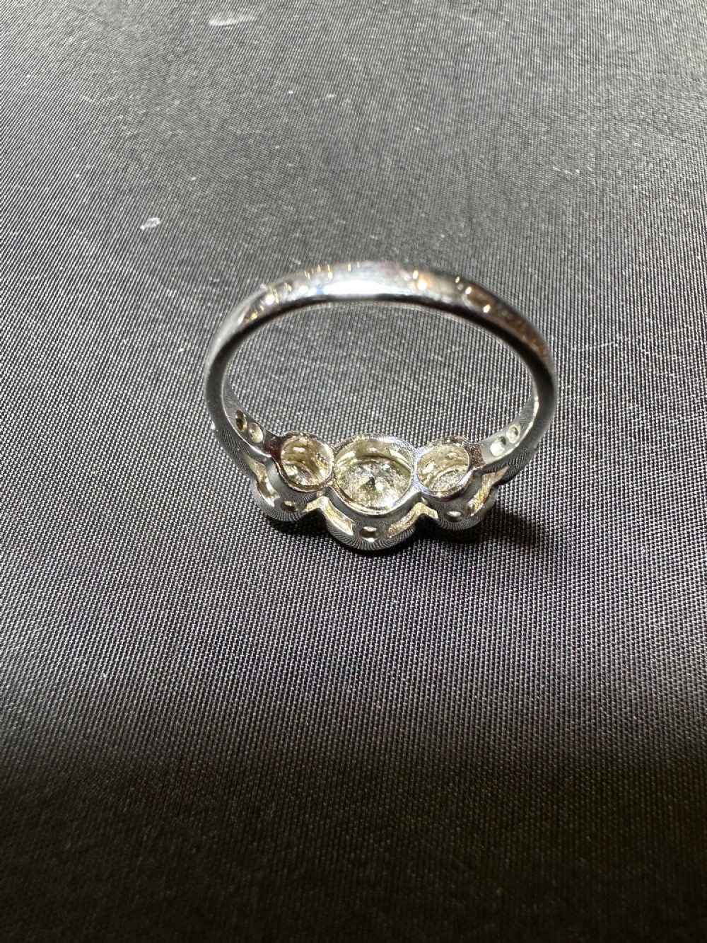 An 18ct white gold trinity ring featuring three round brilliant diamonds in rub-over bezel settings with millegrain edging. View II