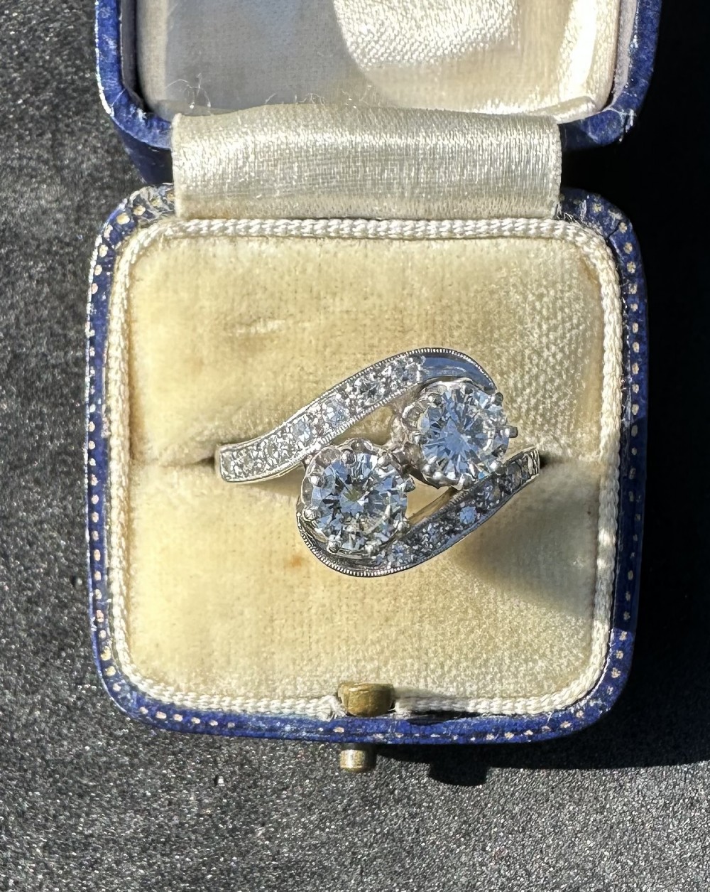 A vintage 14ct white gold double twist ring featuring two central round diamonds encircled by pave-set diamond accents with milgrain detailing.