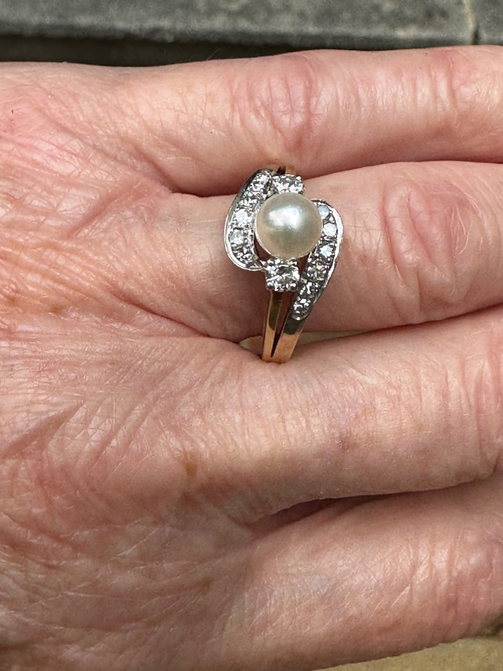 A 14ct gold crossover ring featuring a single central white pearl flanked by sweeping diamond-set bypass shoulders. View VI