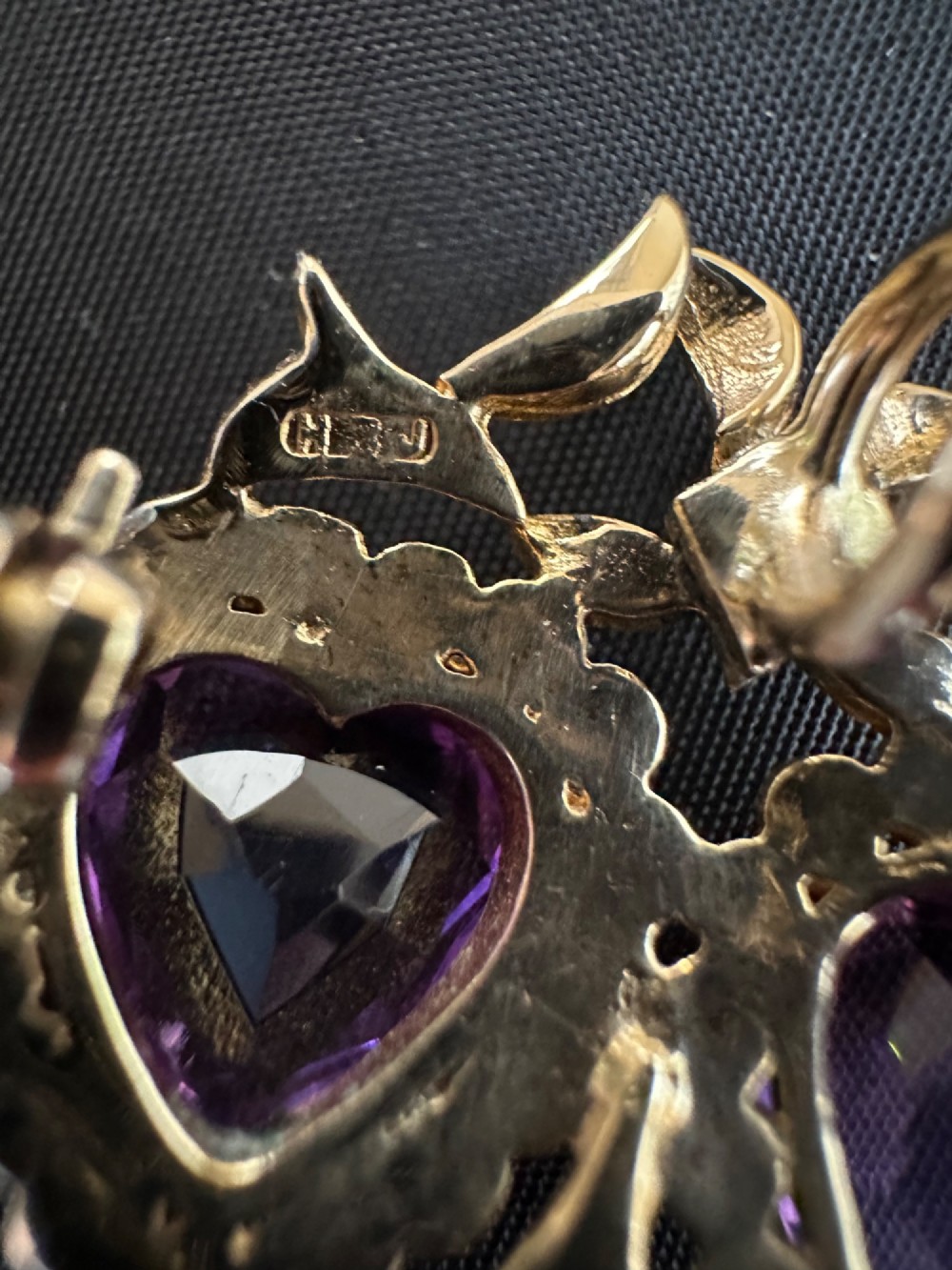 An antique 9ct gold double heart brooch set with two faceted purple amethysts surrounded by seed pearls and topped with a ribbon bow motif. View V