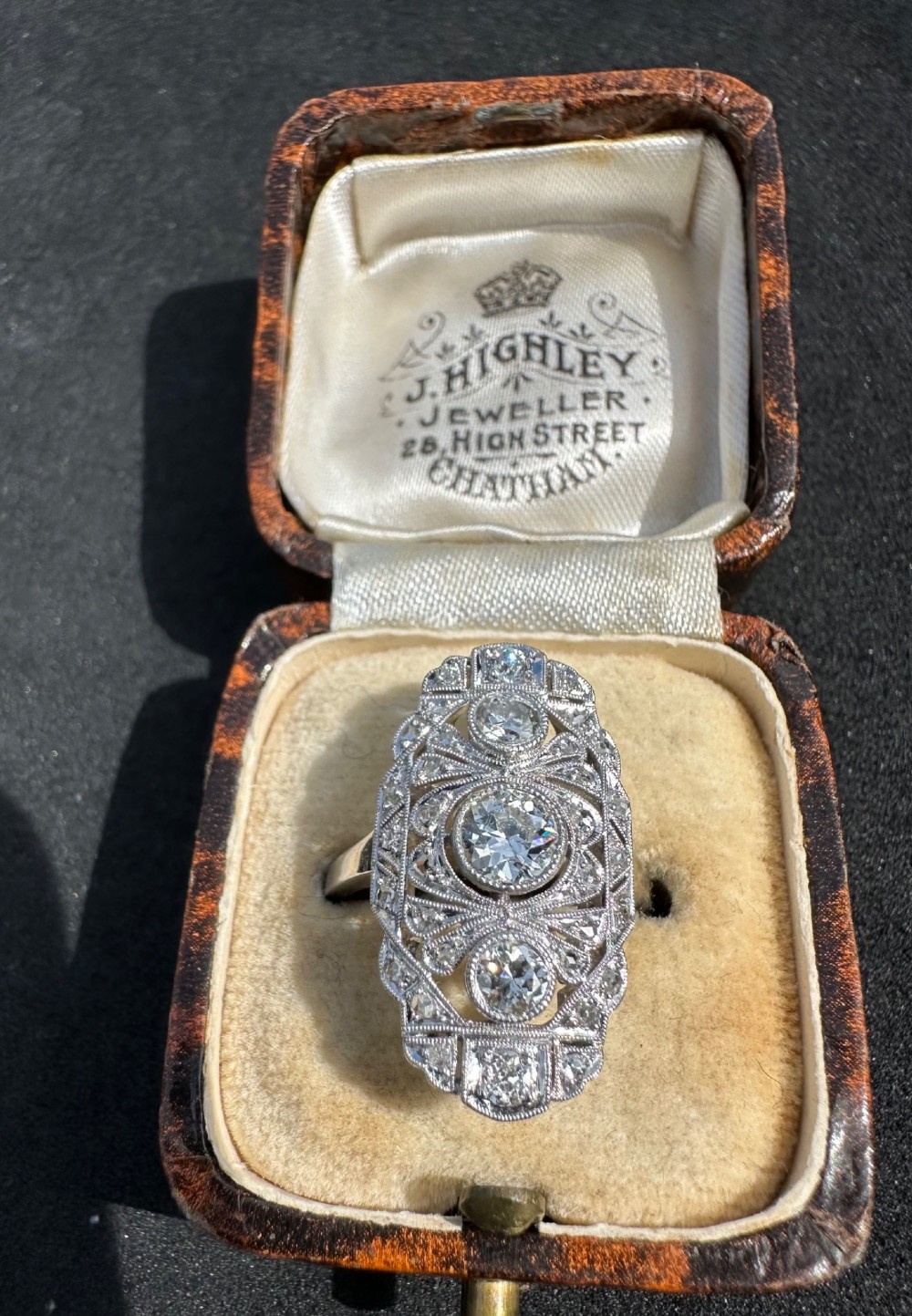 An Art Deco platinum panel ring featuring an elongated geometric openwork design set with multiple circular diamonds and milgrain detailing. View II