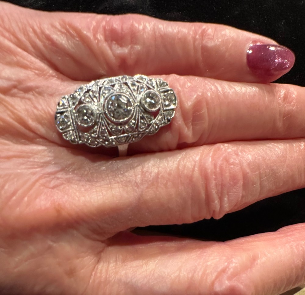 An Art Deco platinum panel ring featuring an elongated geometric openwork design set with multiple circular diamonds and milgrain detailing. View III