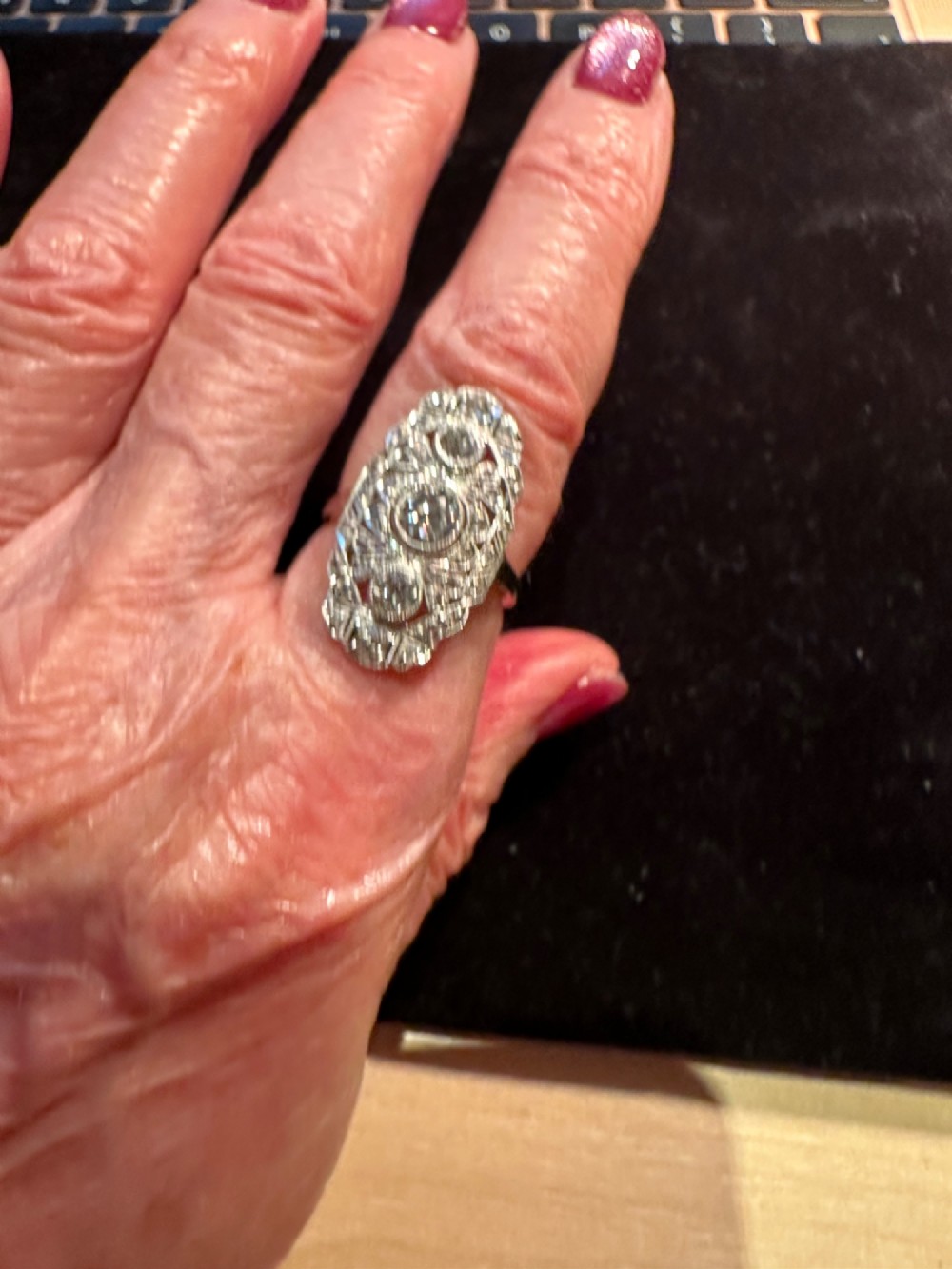 An Art Deco platinum panel ring featuring an elongated geometric openwork design set with multiple circular diamonds and milgrain detailing. View IV