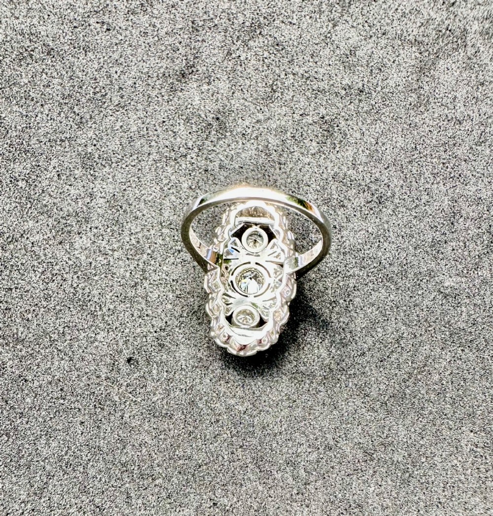 An Art Deco platinum panel ring featuring an elongated geometric openwork design set with multiple circular diamonds and milgrain detailing. View VI