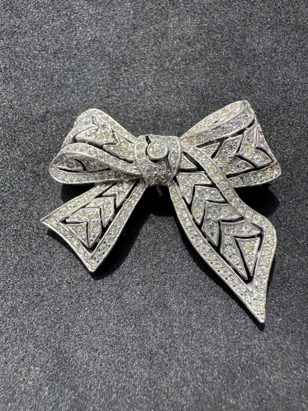 A silver-toned metal bow brooch encrusted with clear paste stones arranged in a geometric openwork pattern.