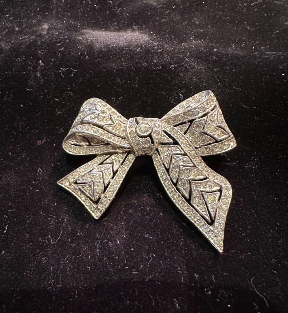 A silver-toned metal bow brooch encrusted with clear paste stones arranged in a geometric openwork pattern. View IV