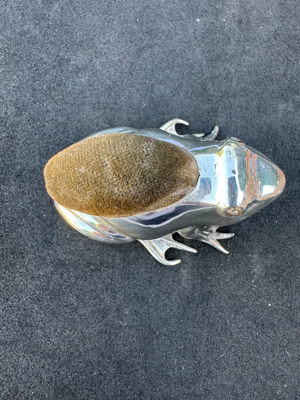 An Edwardian sterling silver pin cushion cast in the shape of a frog with an embedded brown fabric cushion on its back.