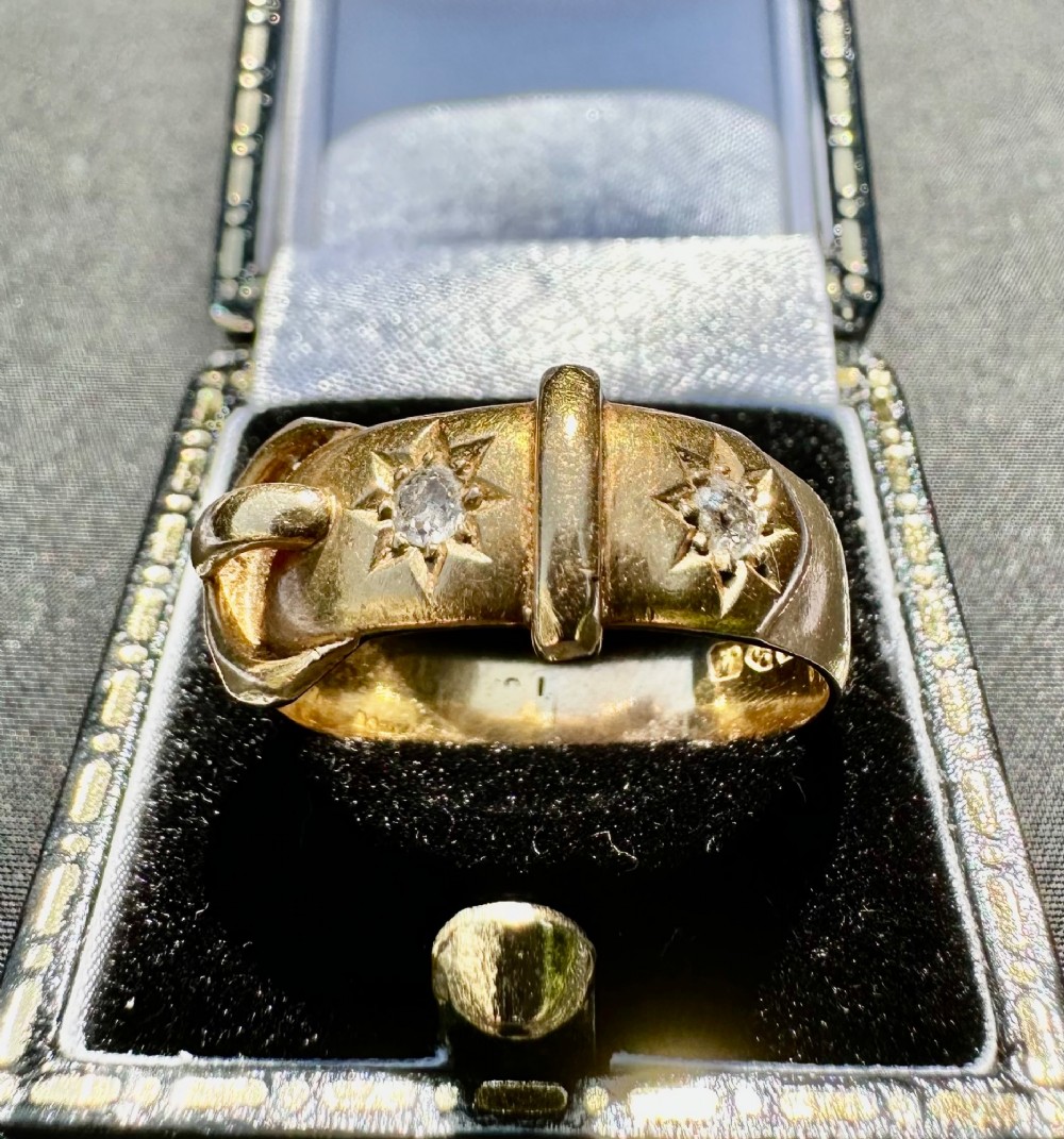 An 18 carat yellow gold band styled as a buckle motif with two star-set diamonds embedded on the surface.