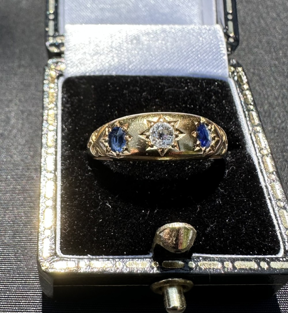 An antique 18ct yellow gold gypsy ring featuring a central diamond and two flanking blue sapphires set into carved starburst mounts.