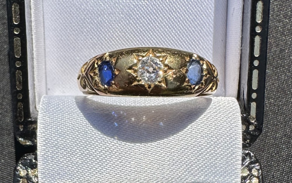 An antique 18ct yellow gold gypsy ring featuring a central diamond and two flanking blue sapphires set into carved starburst mounts. View II