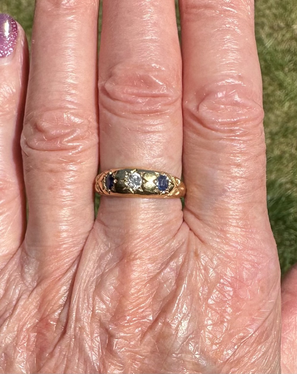 An antique 18ct yellow gold gypsy ring featuring a central diamond and two flanking blue sapphires set into carved starburst mounts. View V