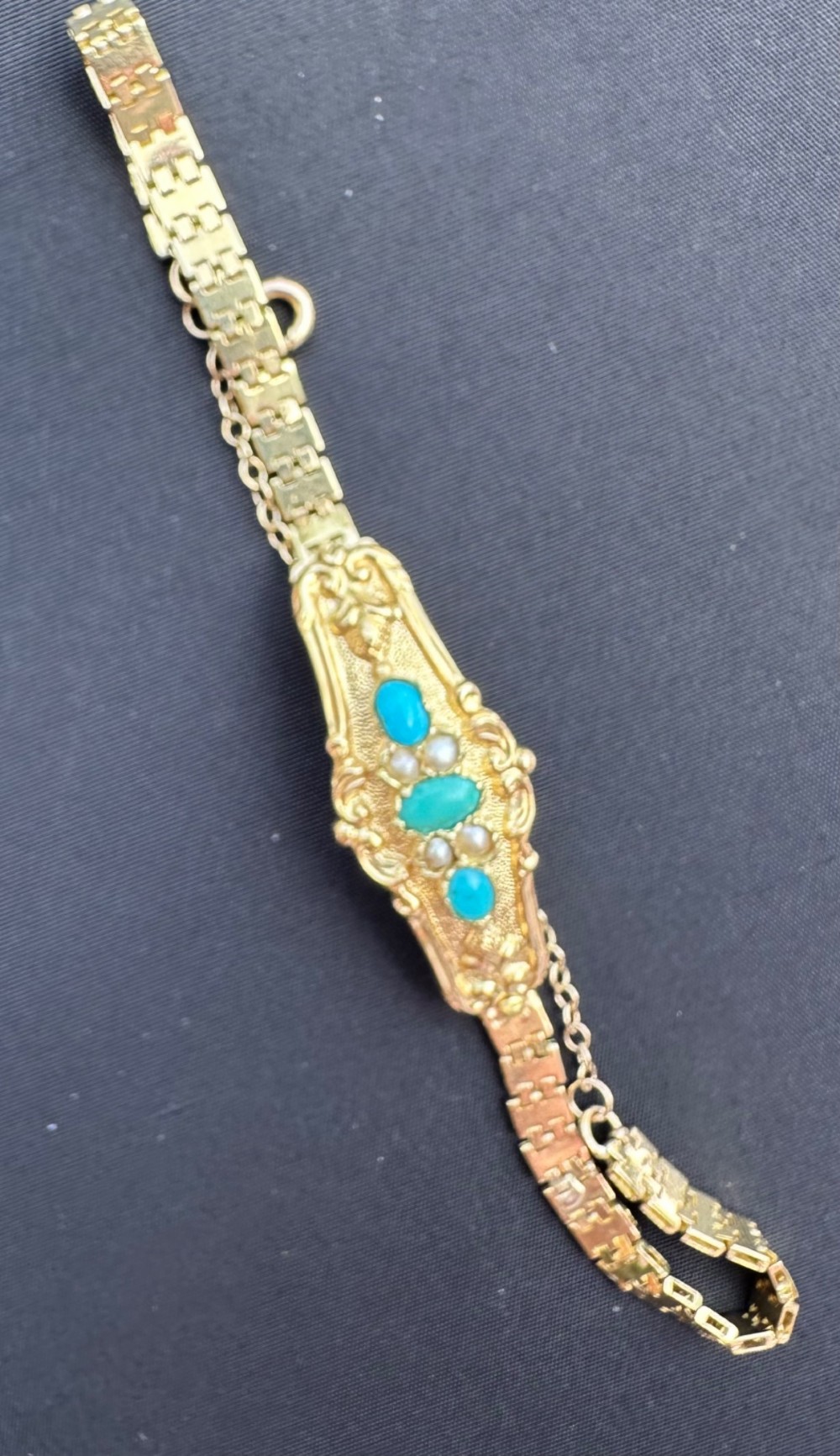 An antique 18ct gold bracelet featuring an ornate central panel set with three turquoise cabochons and seed pearls attached to a flexible gold link strap. View II