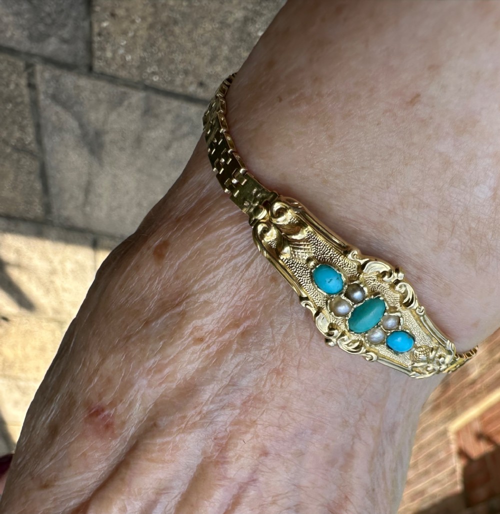 An antique 18ct gold bracelet featuring an ornate central panel set with three turquoise cabochons and seed pearls attached to a flexible gold link strap. View IV