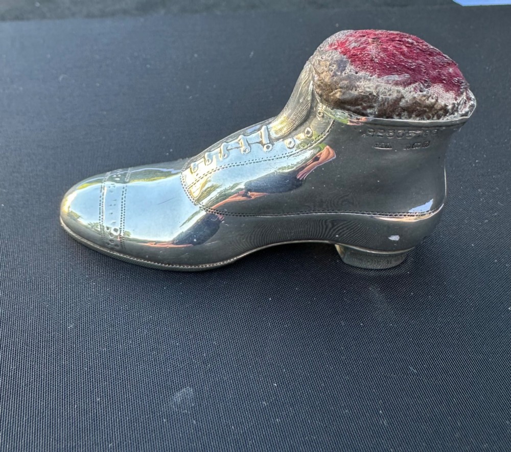 An antique sterling silver pin cushion formed in the shape of a lace-up shoe with a dark red velvet cushion insert.