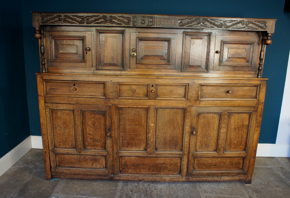 A large 18th-century carved oak court cupboard with recessed upper doors, carved top frieze with initials, and three lower cupboard doors. View III