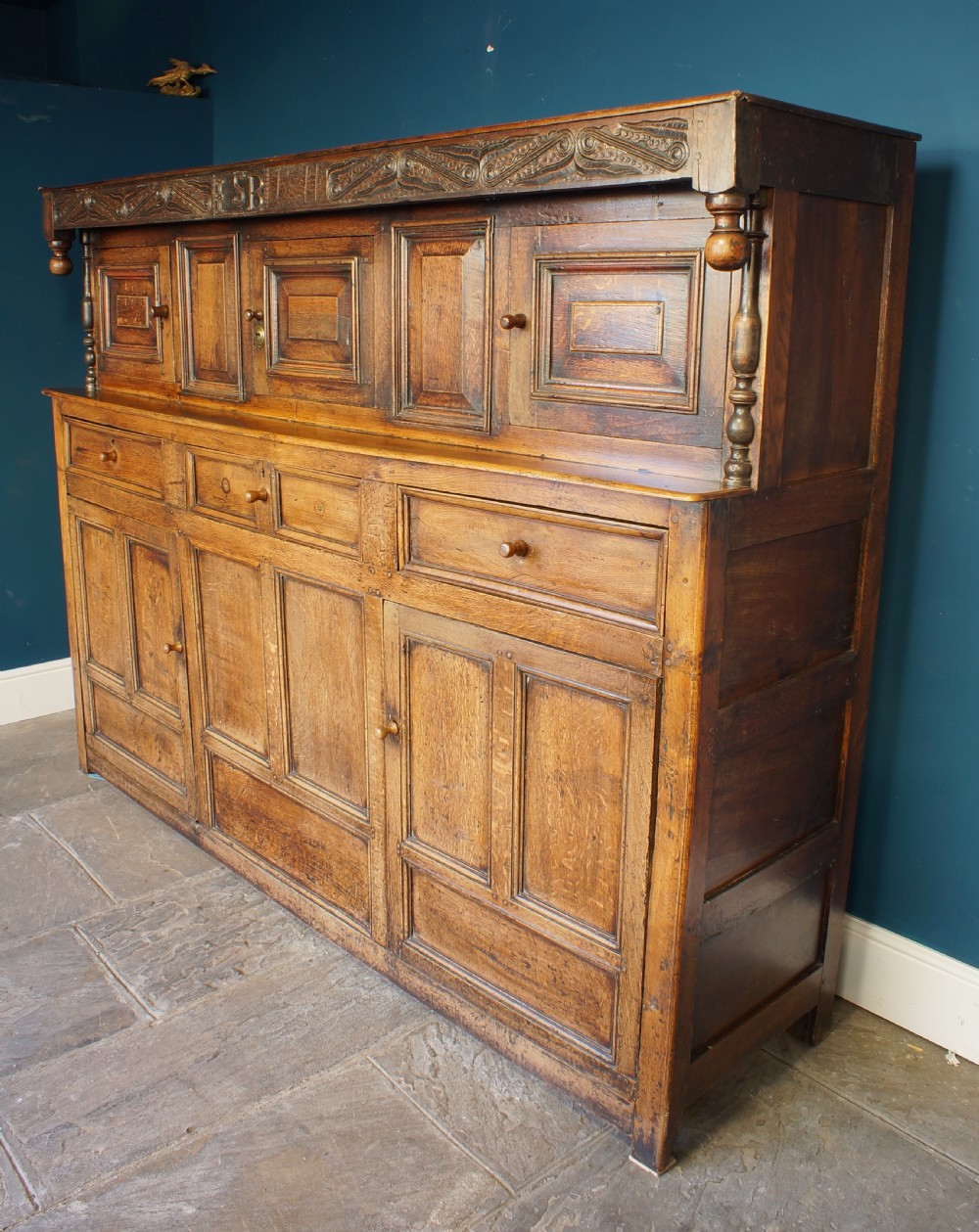 A large 18th-century carved oak court cupboard with recessed upper doors, carved top frieze with initials, and three lower cupboard doors. View V