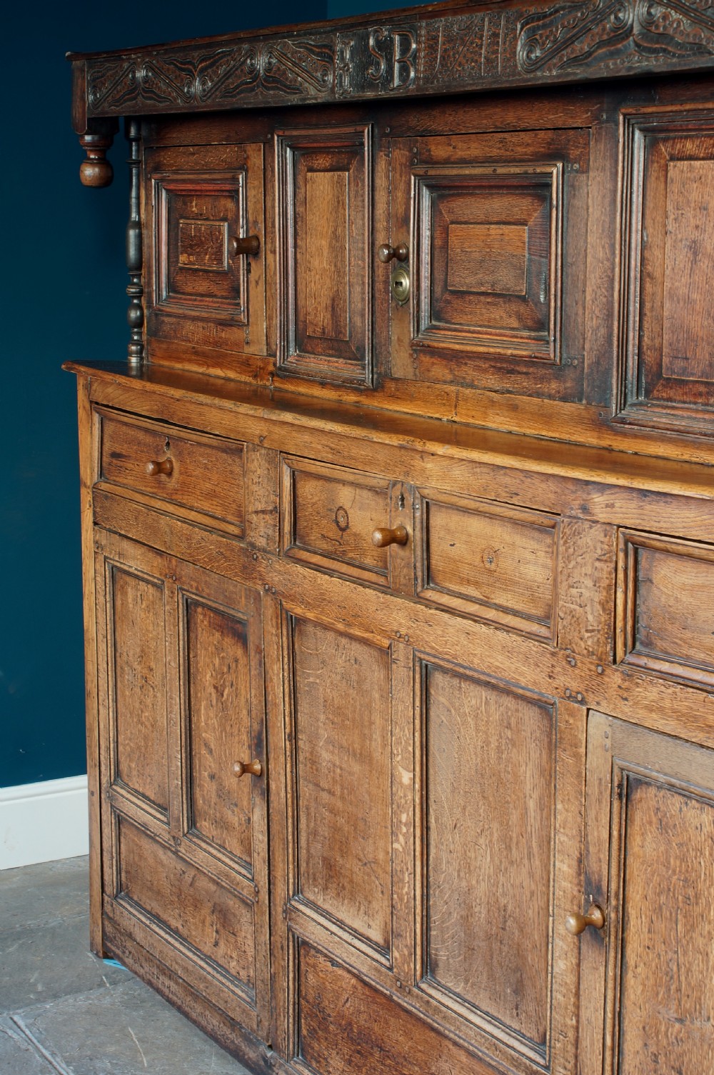 A large 18th-century carved oak court cupboard with recessed upper doors, carved top frieze with initials, and three lower cupboard doors. View VI