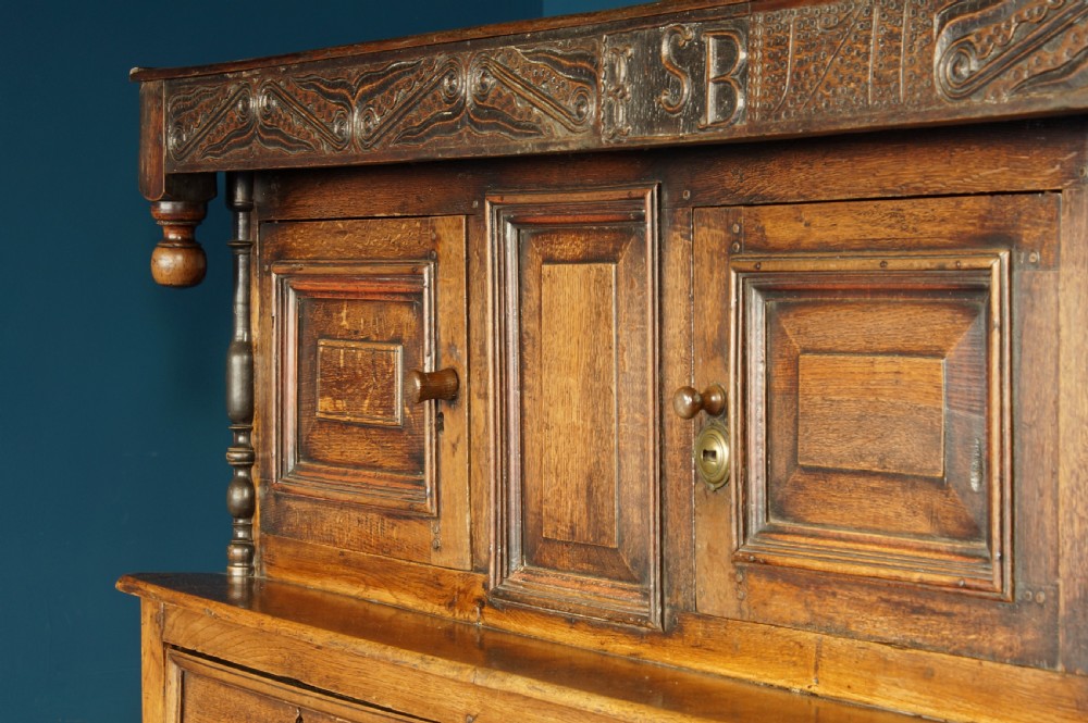 A large 18th-century carved oak court cupboard with recessed upper doors, carved top frieze with initials, and three lower cupboard doors. View VII