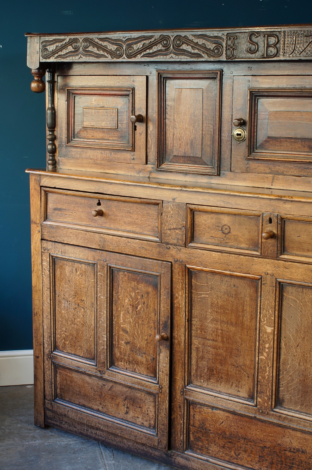 A large 18th-century carved oak court cupboard with recessed upper doors, carved top frieze with initials, and three lower cupboard doors. View X