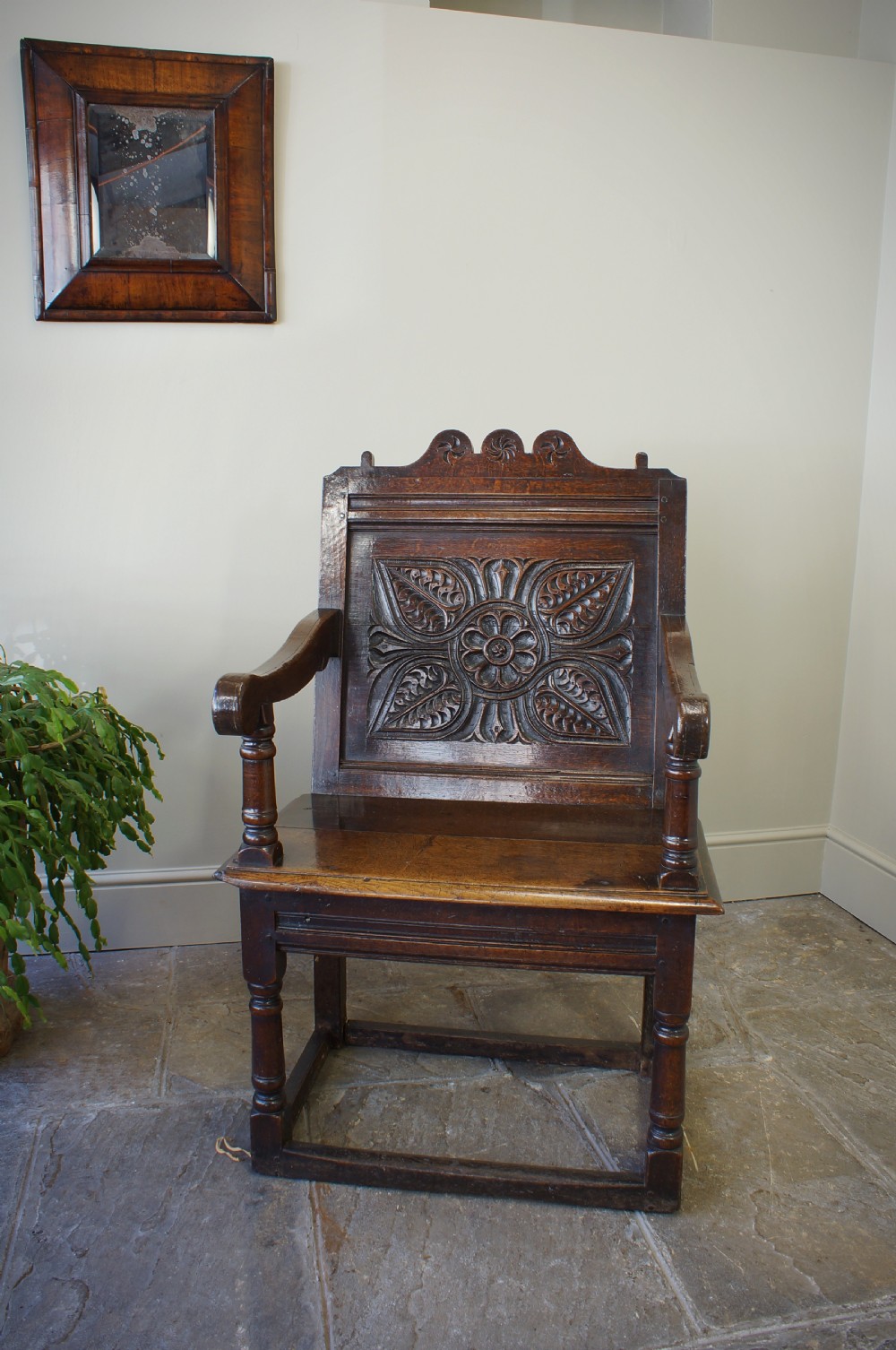 A 17th-century dark oak wainscot armchair with a deeply carved back panel, turned front legs, and sturdy box stretchers. View V