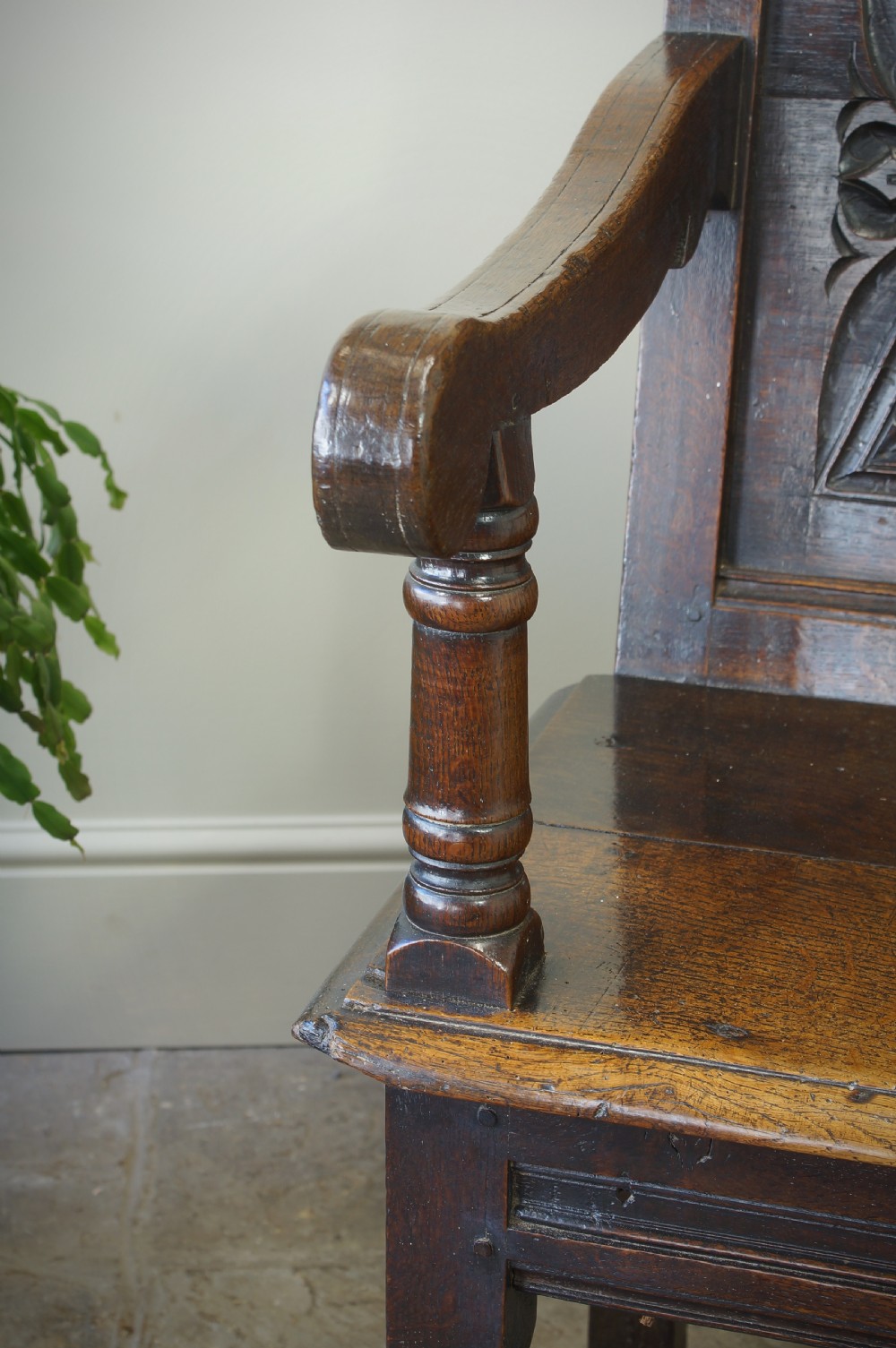 A 17th-century dark oak wainscot armchair with a deeply carved back panel, turned front legs, and sturdy box stretchers. View VI